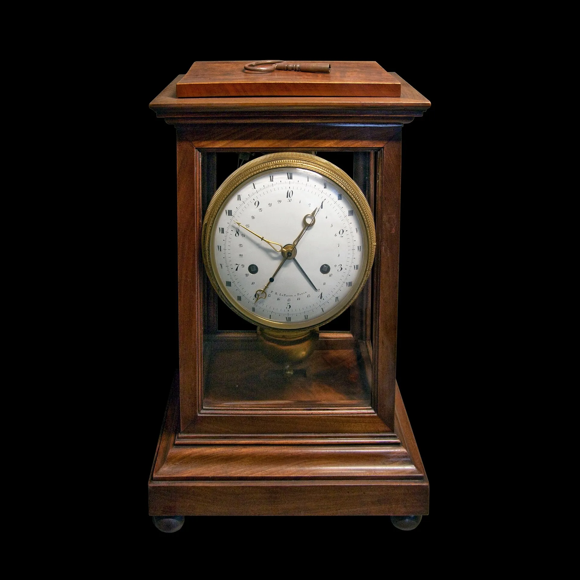 A wooden mantel clock with a white dial showing decimal hours.